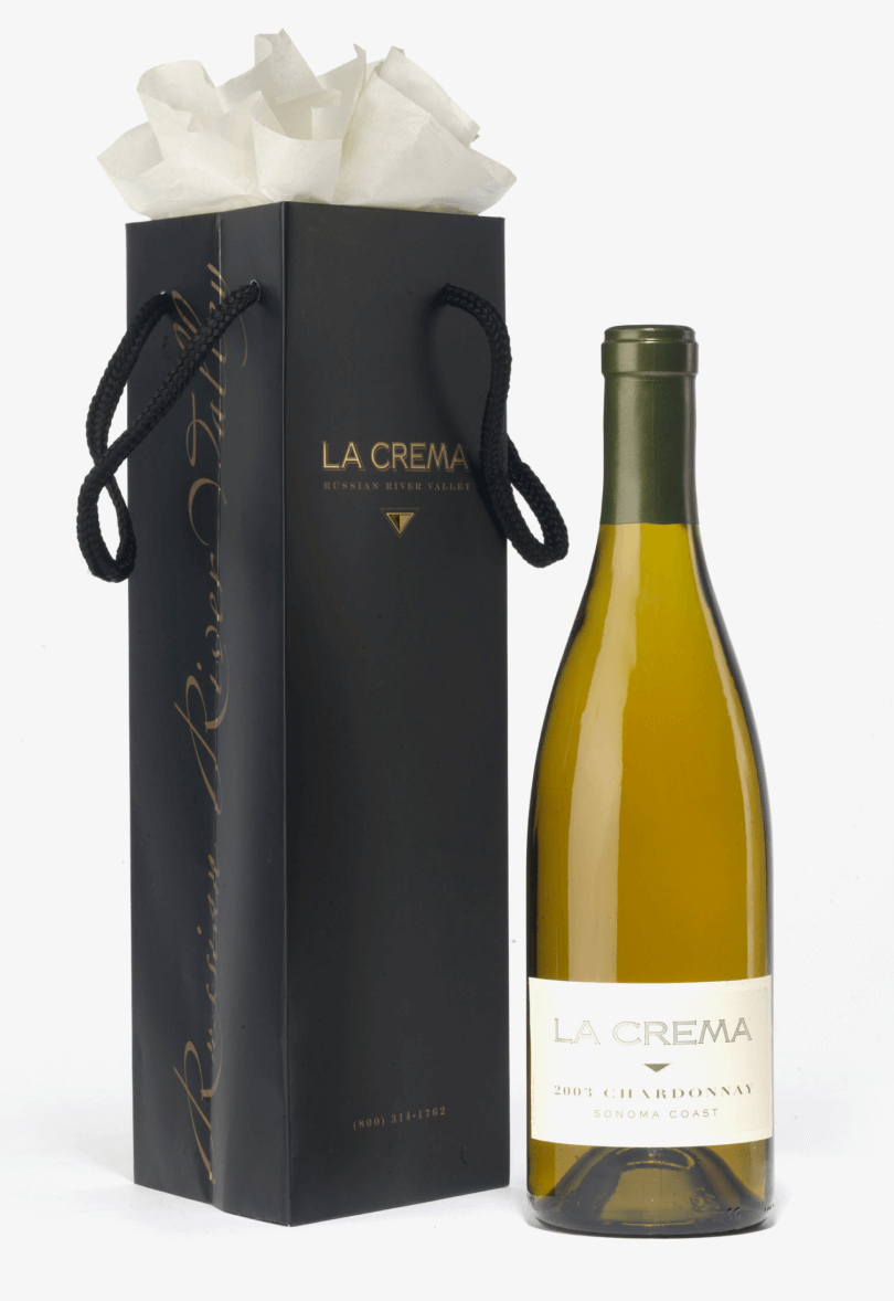 A bottle of white wine next to a black gift bag with elegant packaging.
